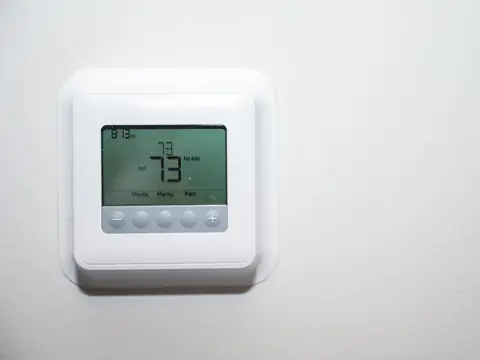 A white programmable thermostat on a white wall, its screen set to cool and reading 73 degrees